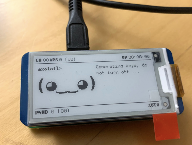 Picture of a raspberry pi with an e-ink display showing a little smiling face, some status information and a text Generating keys, do not turn off.